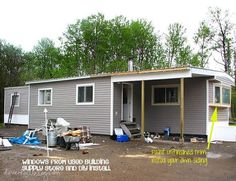 a small gray house sitting in the middle of a yard next to trees and other items