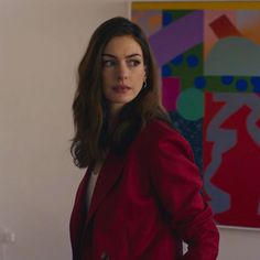 a woman standing in front of a painting wearing a red blazer and white shirt