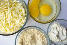 four bowls containing eggs, cheese and other ingredients on a white counter top with one egg in the middle