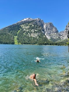 two people swimming in the water near mountains