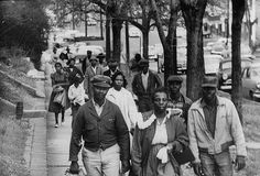 an old black and white photo of people walking down the street in front of trees