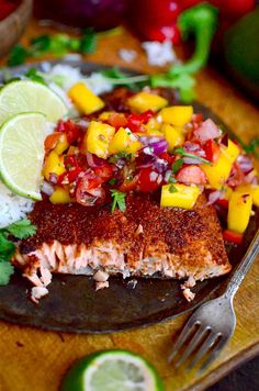 a piece of salmon with mango salsa on a plate next to a fork and lime wedges