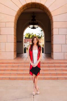 a woman standing in front of an archway wearing a red jacket and white dress with heels