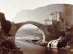 an old photo of a bridge over a river with a castle on the other side