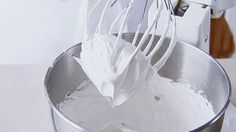 a whisk is being used to mix white cream in a mixing bowl with a mixer attachment