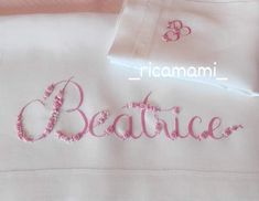 embroidered name on white shirt with pink trimmings and flower design in the center