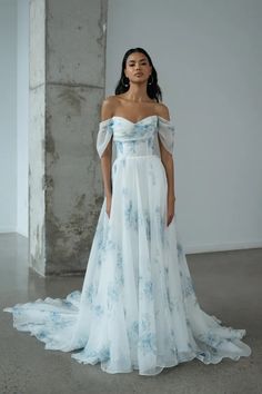 a woman in a white and blue dress standing next to a columned wall wearing an off - the - shoulder gown