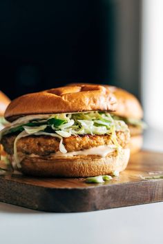 two chicken burgers sitting on top of a wooden cutting board next to each other