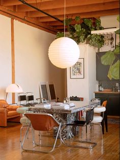 a dining room table with chairs and a lamp hanging from it's ceiling in front of a couch