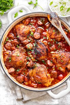 a large pot filled with meat and vegetables on top of a white cloth next to a wooden spoon