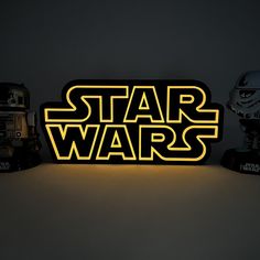 the star wars logo is lit up in yellow and black colors, with two helmets behind it