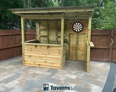 a wooden bar with darts on it in the middle of a patio next to a fence