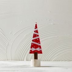 a small red and white christmas tree sitting on top of a wooden block in front of a white wall