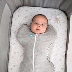 a baby laying in a crib wearing a grey and white blanket