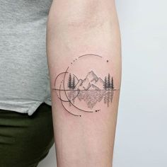 a person with a tattoo on their arm has a mountain and trees in the background