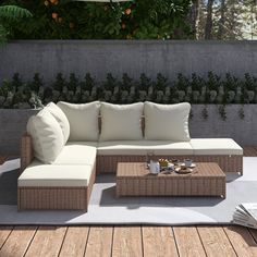 an outdoor couch and coffee table on a wooden deck with plants in the back ground