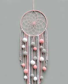 a pink and white crochet dream catcher hanging on a wall next to a gray wall