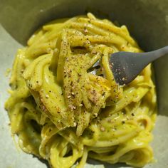 a bowl filled with pasta covered in pesto and seasoning next to a spoon