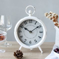 an alarm clock sitting on top of a wooden table next to a vase with flowers