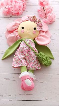 a doll laying on top of a wooden floor next to pink flowers and green leaves