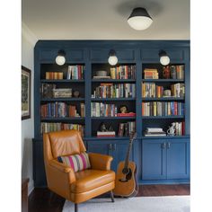 a living room with blue bookcases and a guitar in the chair next to it