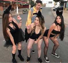 three girls in bunny costumes posing on the street with one girl pointing at her phone