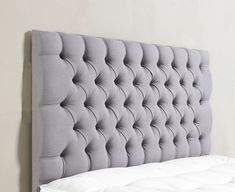 an upholstered headboard with white sheets and pillows on a bed in a bedroom