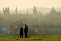 two people standing on top of a lush green field next to a tall city skyline