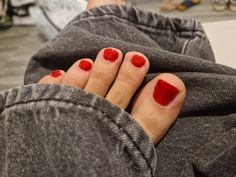 a person with red nail polish on their toes and feet in grey sweats sitting down