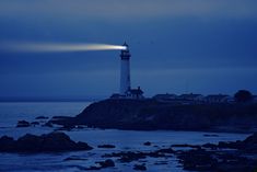 the light house is lit up at night on the rocky shore by the water's edge