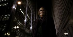 the dark knight joker is standing in front of a building at night with his hands on his hips