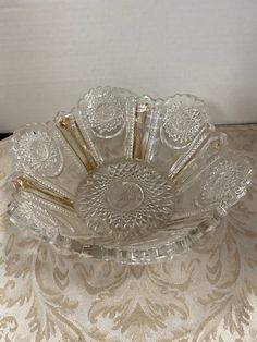 a clear glass bowl with gold handles on a white tablecloth covered table, next to a wall