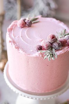 a pink frosted cake with berries and holly on top is sitting on a white pedestal