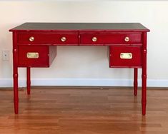 a red desk with two drawers and gold handles on the top, in front of a white wall