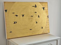 a painting on top of a dresser with birds flying in the sky above it,