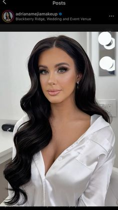 a woman with long black hair wearing a white shirt and posing in front of a mirror