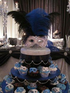 a three tiered cake with blue frosting and cupcakes on the bottom