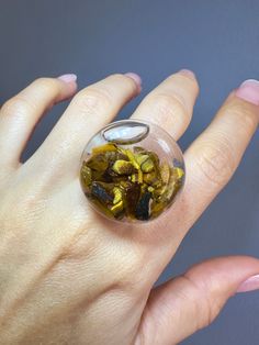 Immerse yourself in nature's magic with this stunning 27mm glass bubble ring. Inside, discover high-quality natural tiger's eye crystals, carefully encapsulated in liquid with subtle glittery flakes that dance with every movement. This unique 27mm ring shaker is not only a dazzling piece of jewelry but also a conversation starter that is sure to capture attention. Tiger's eye is revered for its believed ability to bring protection, confidence, and mental clarity, making this ring a meaningful and beneficial choice. Choose elegance and uniqueness with this beautiful ring that embodies nature's beauty at its finest. Note: It is recommended to avoid damage on the ring since the surface is glass Additionally, explore my other listings, and enjoy free shipping on all orders over $35! ❤Each jewe Unique Clear Crystal Ring For Gift, Unique Clear Crystal Ring As A Gift, Unique Clear Rings, Unique Clear Round Rings, Unique Cabochon Crystal Ring, Unique Round Cabochon Crystal Ring, Amber Crystal Ring Gift, Eye Crystals, Tigers Eye Ring