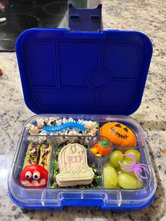 a blue plastic container filled with food on top of a marble counter next to oranges and grapes