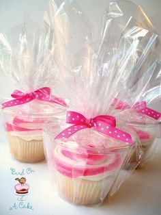 three cupcakes wrapped in plastic with pink bows