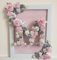 the letter m made out of flowers is displayed in front of a pink wall frame