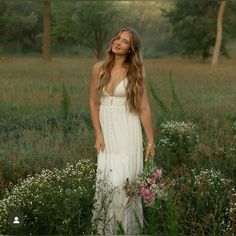 a beautiful woman in a white dress standing in the middle of a field with wildflowers