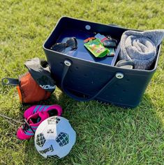 a blue cooler sitting on top of a lush green field next to sports gear and socks