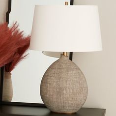 a white lamp sitting on top of a wooden table next to a mirror and a red feather