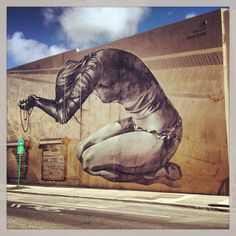 a large mural on the side of a building with a woman kneeling down holding a hose