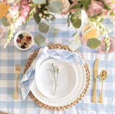 the table is set with plates, silverware, and flowers on blue gingham cloth