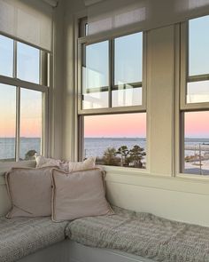 a window seat with two pillows on it in front of some windows overlooking the ocean