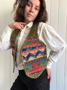 a woman wearing a colorful vest and white shirt posing for the camera with her hands on her hips