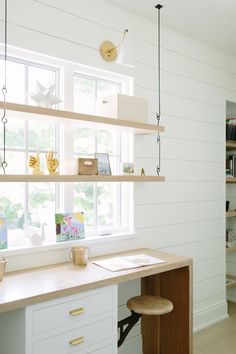 a home office with white walls and wooden shelves on the wall, along with an open window