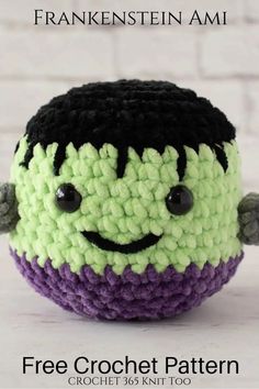 a crocheted toy with black eyes and green, purple, and white stripes